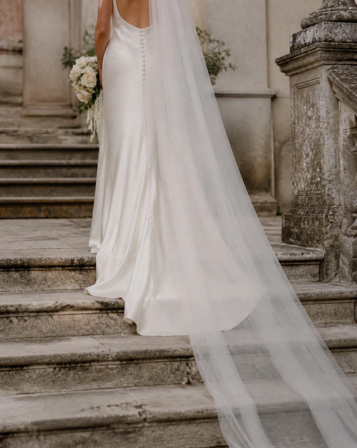 Silk wedding gown and veil trailing down stone steps